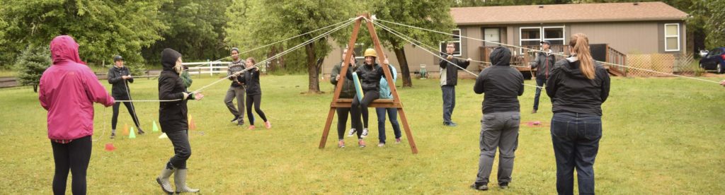 High school campers solving a challenge course puzzle involving a wooden frame and thin ropes