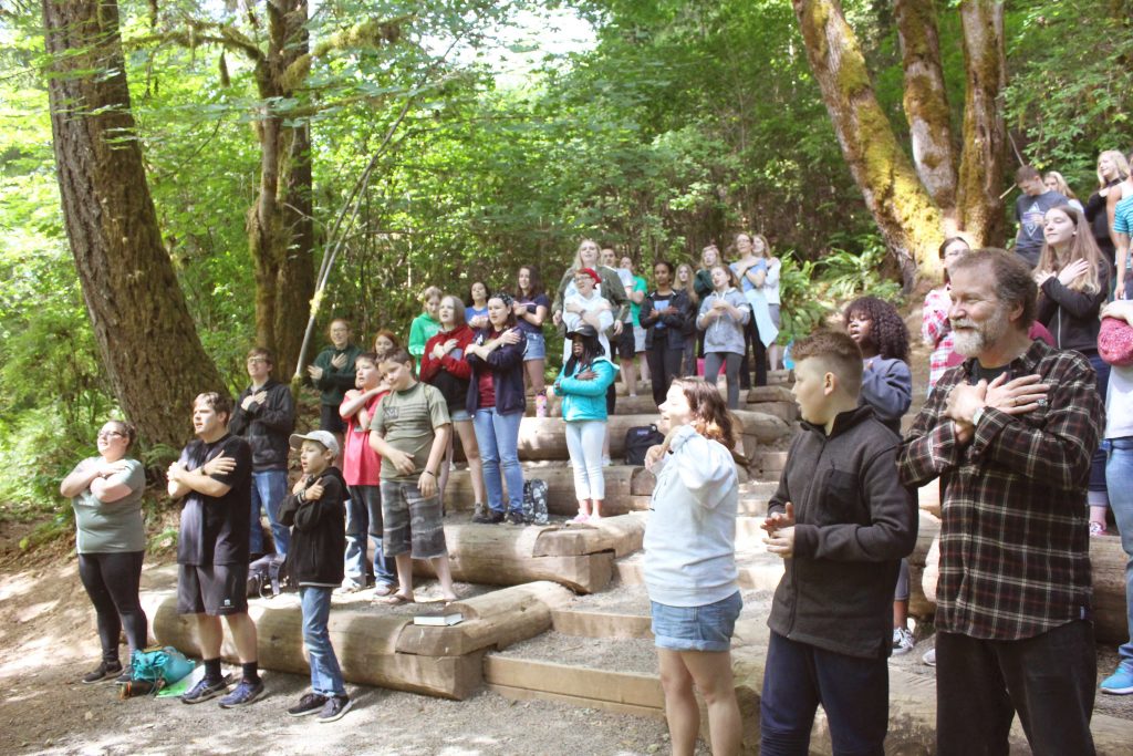Forthy campers and adult leaders singing and doing hand motions at outdoor chapel during Confirmation Camp at Camp Lutherwood Oregon