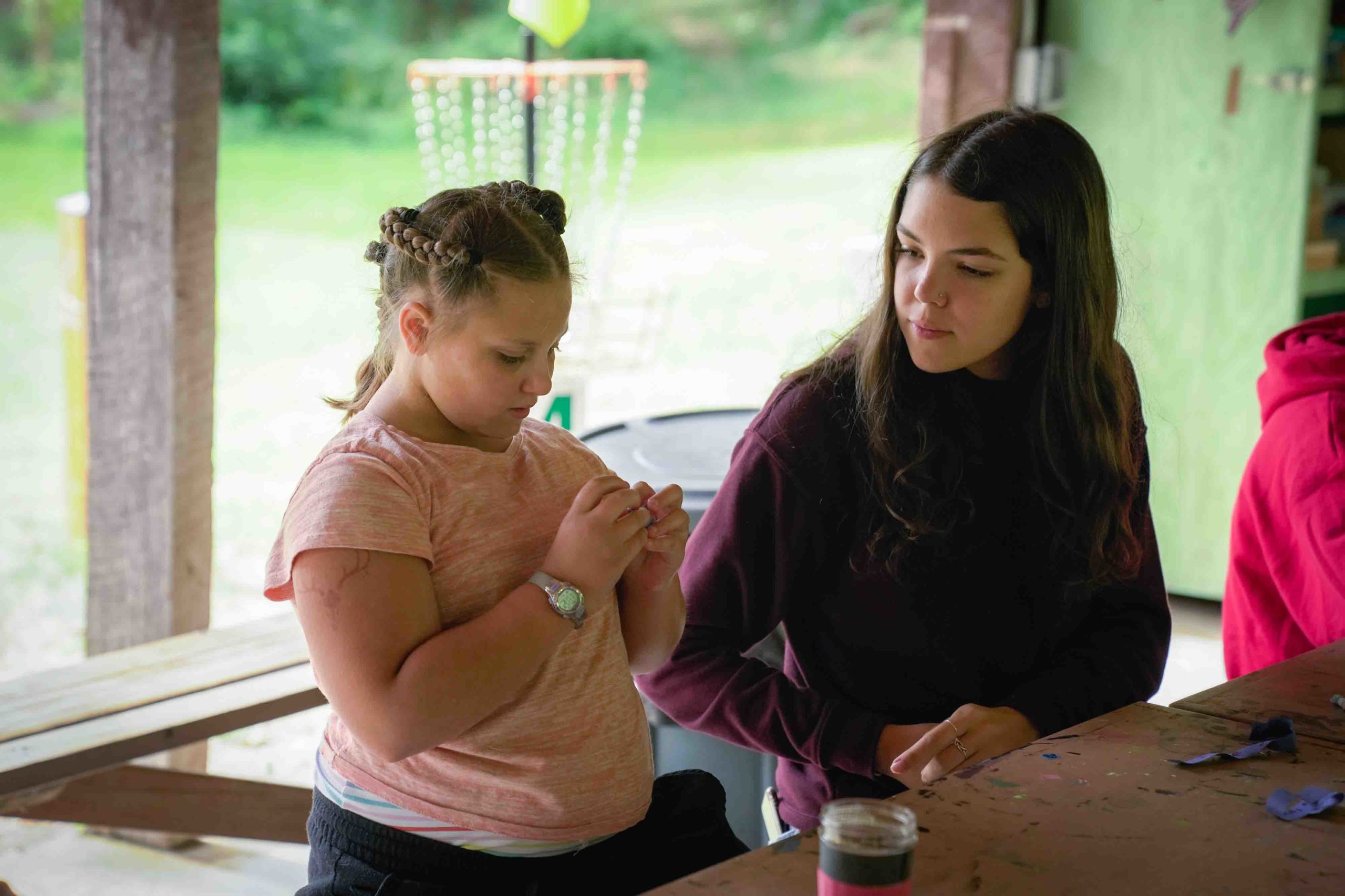 A camp counselor watching a middle-school camper work on a craft in the craft shed