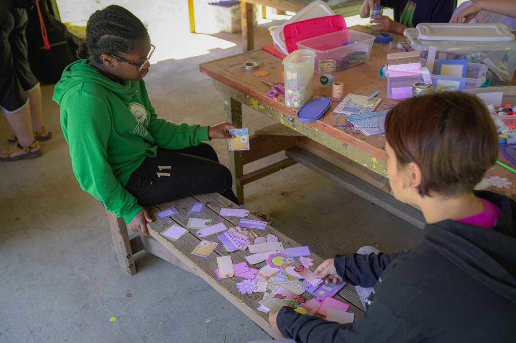 Two female campers sort through craft supplies to work on their project.