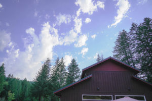 The top of the dining hall at Camp Lutherwood Oregon against a mostly sunny sky and fir trees