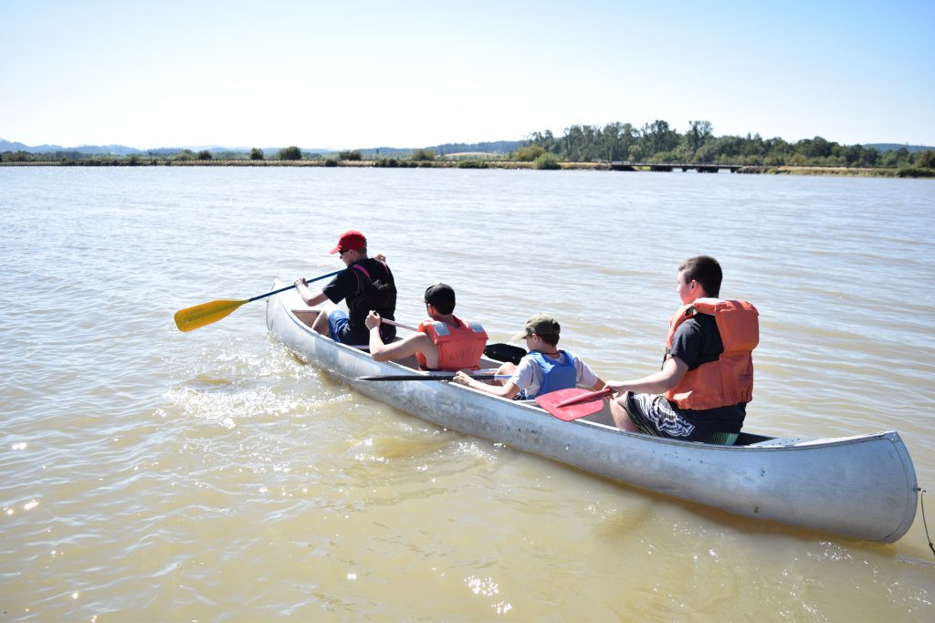 Three campers and a camp counselor rowing a canoe