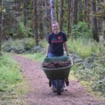 A woman moving a wheelbarrow full of bark chips on a trail at Camp Lutherwood Oregon