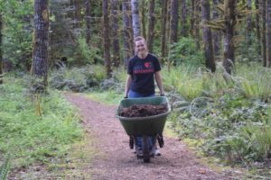 A woman moving a wheelbarrow full of bark chips on a trail at Camp Lutherwood Oregon