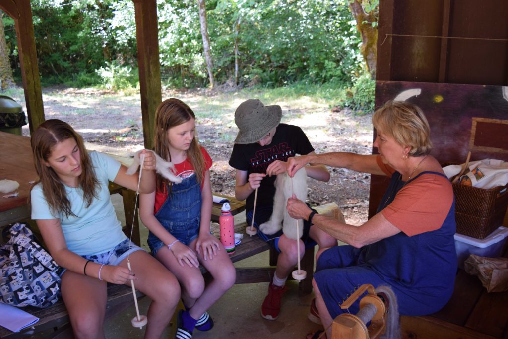 Woman teaching craft time as campers spin wool into thread
