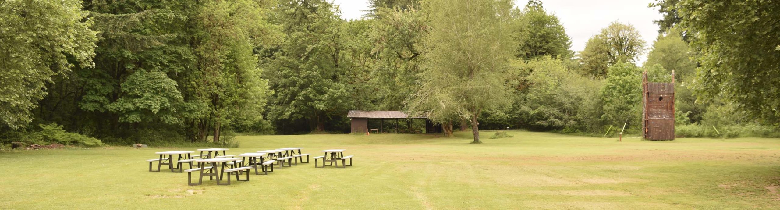 The front field at Camp Lutherwood Oregon with a view of picnic tables, the craft shed, and the climbing wall