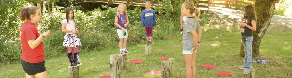 Elementary-age campers standing on posts while participating in a challenge course activity