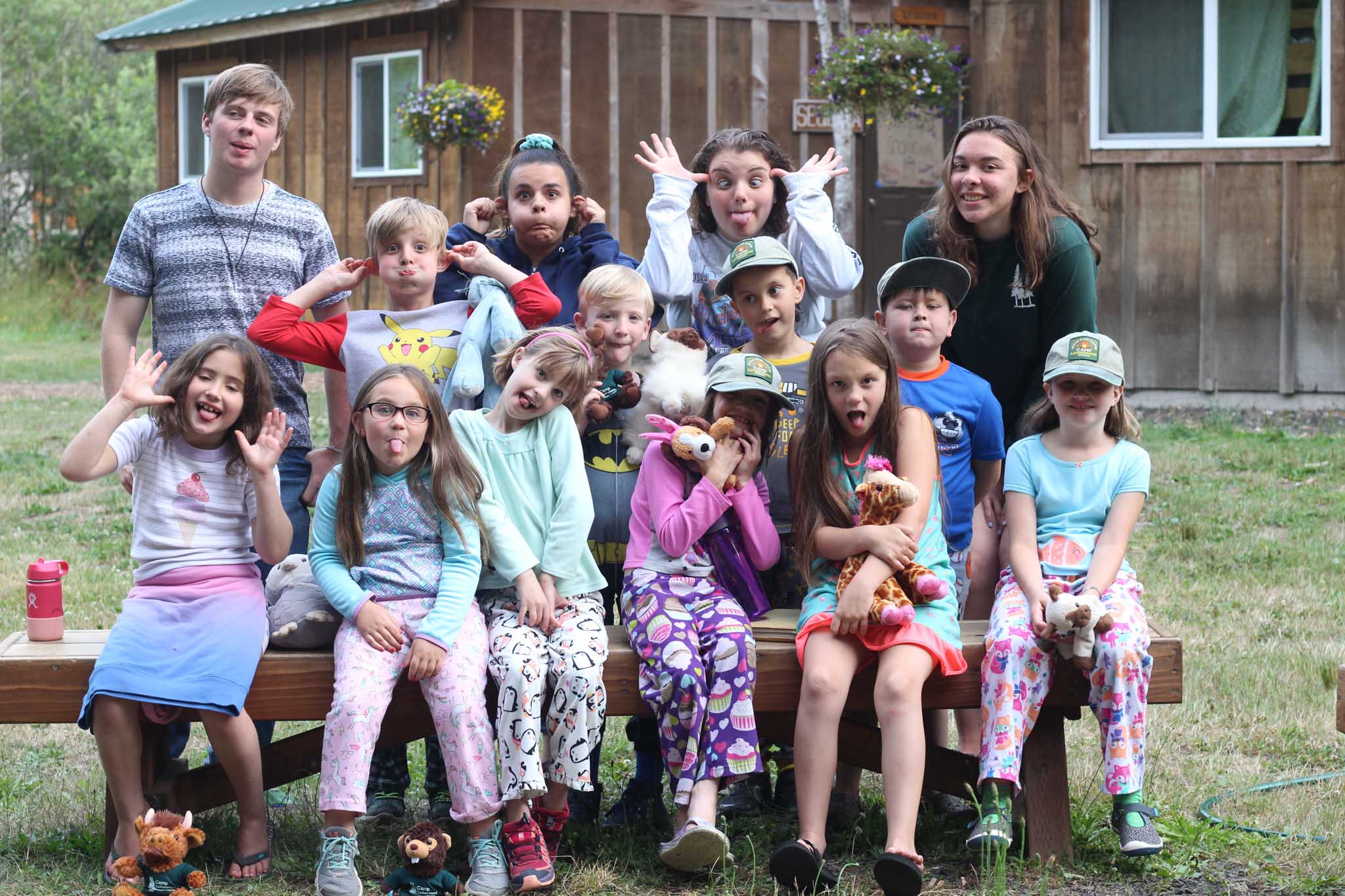 Elementary-age campers with their counselors sitting on a bench and making silly faces at Camp Lutherwood Oregon