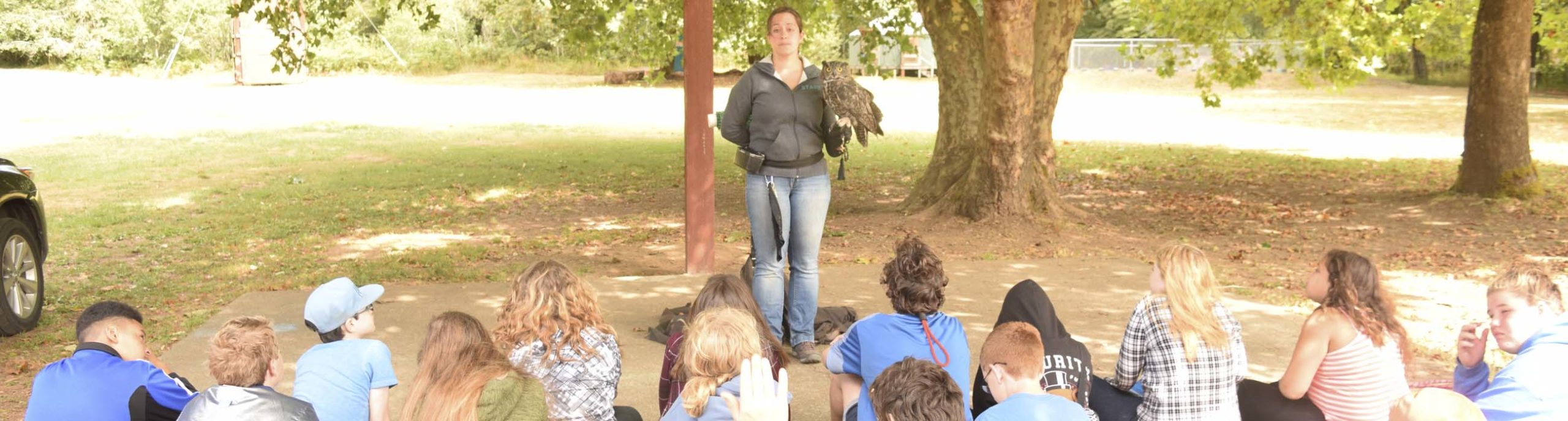A woman teaching campers about raptors with a live owl on her glove