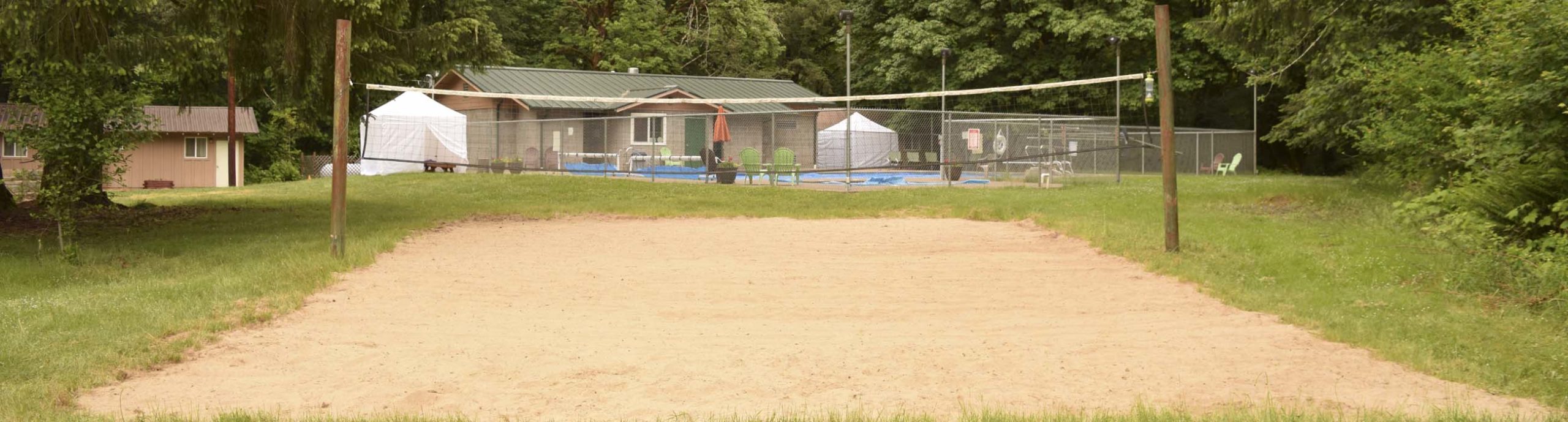 The sand volleyball court with the pool and poolhouse in the background